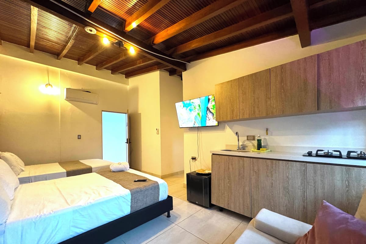 Une chambre d’hôtel moderne équipée d’un lit, d’une petite kitchenette et d’un téléviseur fixé au mur.