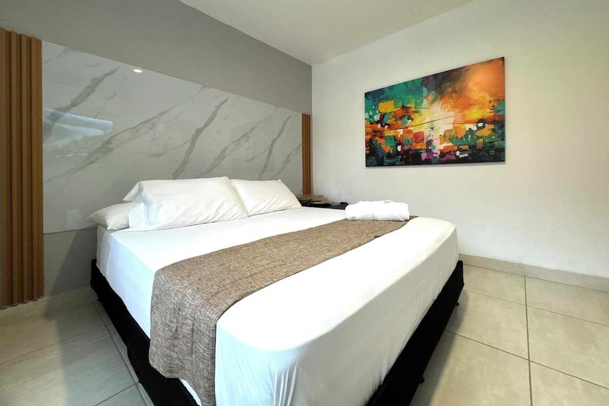 Une chambre d’hôtel avec un grand lit, un mur en marbre et un tableau abstrait aux couleurs vives.