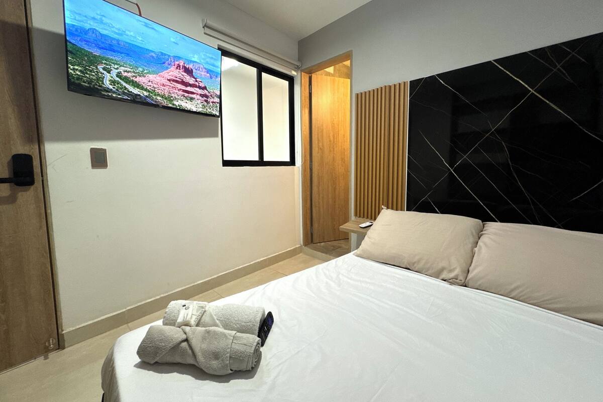 Une chambre d’hôtel avec un lit, un téléviseur fixé au mur et une porte en bois.