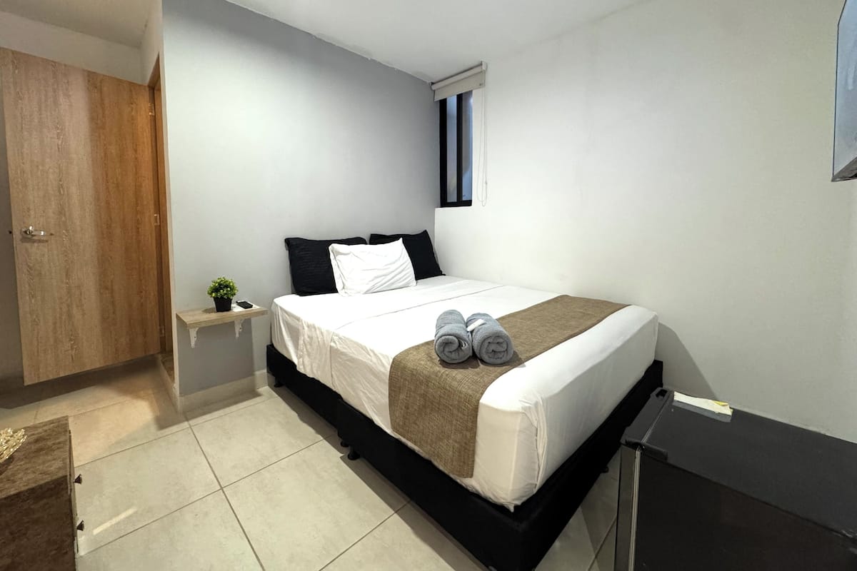 Une chambre moderne avec un lit, une petite table de chevet, une commode, une armoire en bois et une fenêtre.