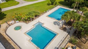 A large outdoor swimming pool with a hot tub and a separate pool area, surrounded by palm trees and a well-maintained lawn.