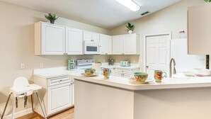 A modern kitchen with white cabinets, a microwave, a coffee maker, and a child’s high chair.