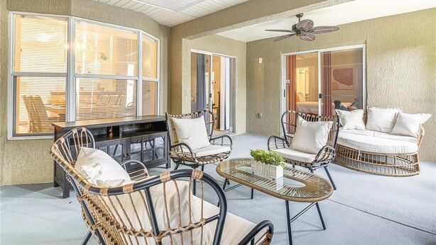 A sunlit patio area with wicker furniture, a glass-top table, and a ceiling fan.