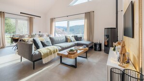 A modern living room with a sectional sofa, a coffee table, and a TV mounted on the wall. - L’Alma - Magnifique maison avec jacuzzi (Gérardmer)