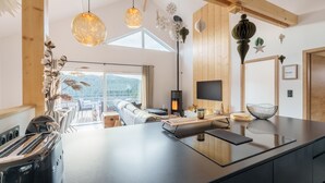 A modern kitchen with a large island, a wood-burning stove, and pendant lighting. - L’Alma - Magnifique maison avec jacuzzi (Gérardmer)
