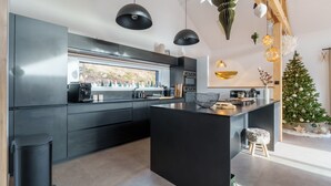 A modern kitchen with dark cabinetry, a central island, pendant lighting, and a decorated Christmas tree. - L’Alma - Magnifique maison avec jacuzzi (Gérardmer)