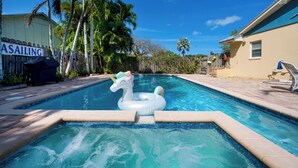 Ein Swimmingpool mit einem Einhorn-Schwimmding, Palmen und einem Gebäude mit der Aufschrift 'SAILING'.