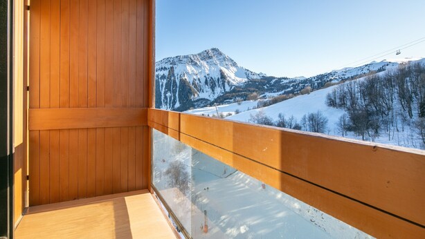 A balcony with a wooden floor and railing, offering a view of a snow-covered mountain range and a clear sky.