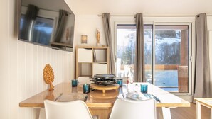 A dining area with a wooden table, white chairs, a grill, and a view of a snowy landscape through large windows.