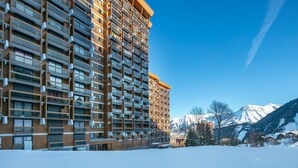 A high-rise hotel with multiple balconies, a snowy landscape, and mountains in the background.