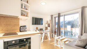 A modern kitchen with a built-in oven, a dining area with a white table and chairs, and a large window with a view of the outdoors.