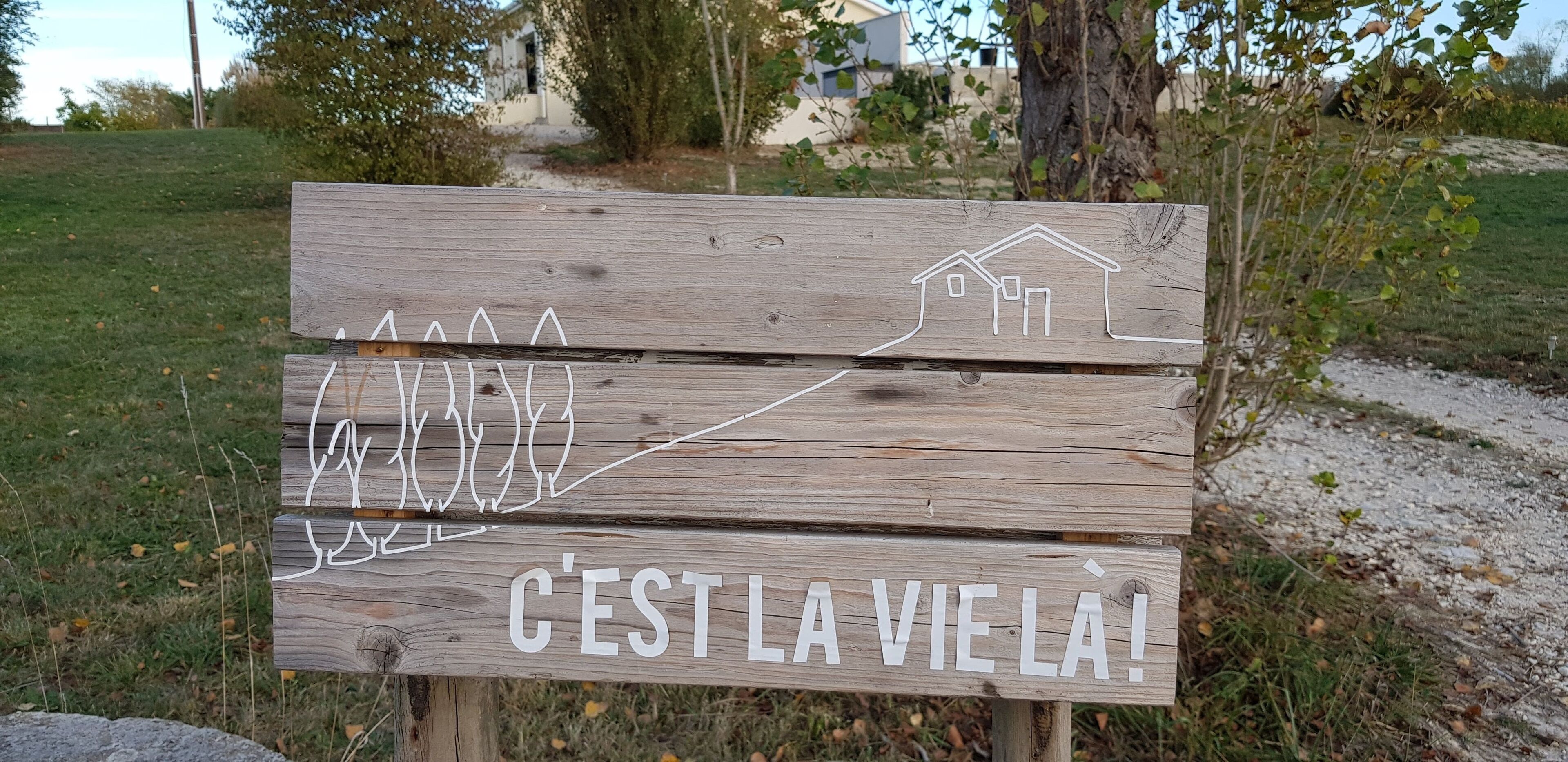 Een houten bord met een silhouet van een huis en de tekst 'C'EST LA VIE LA!'