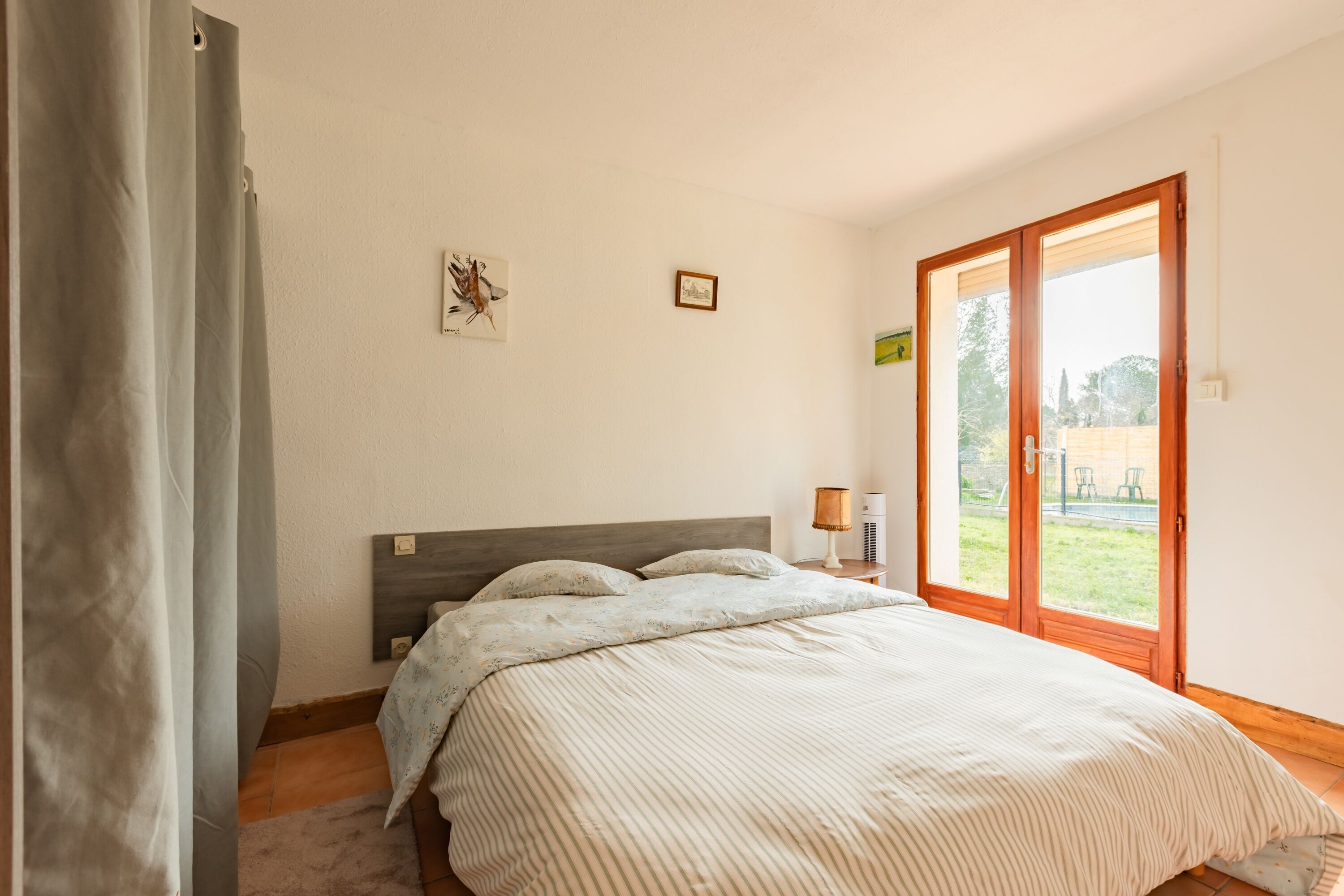 A bedroom with a bed, a nightstand, a lamp, and a view of the outdoors through a glass door.