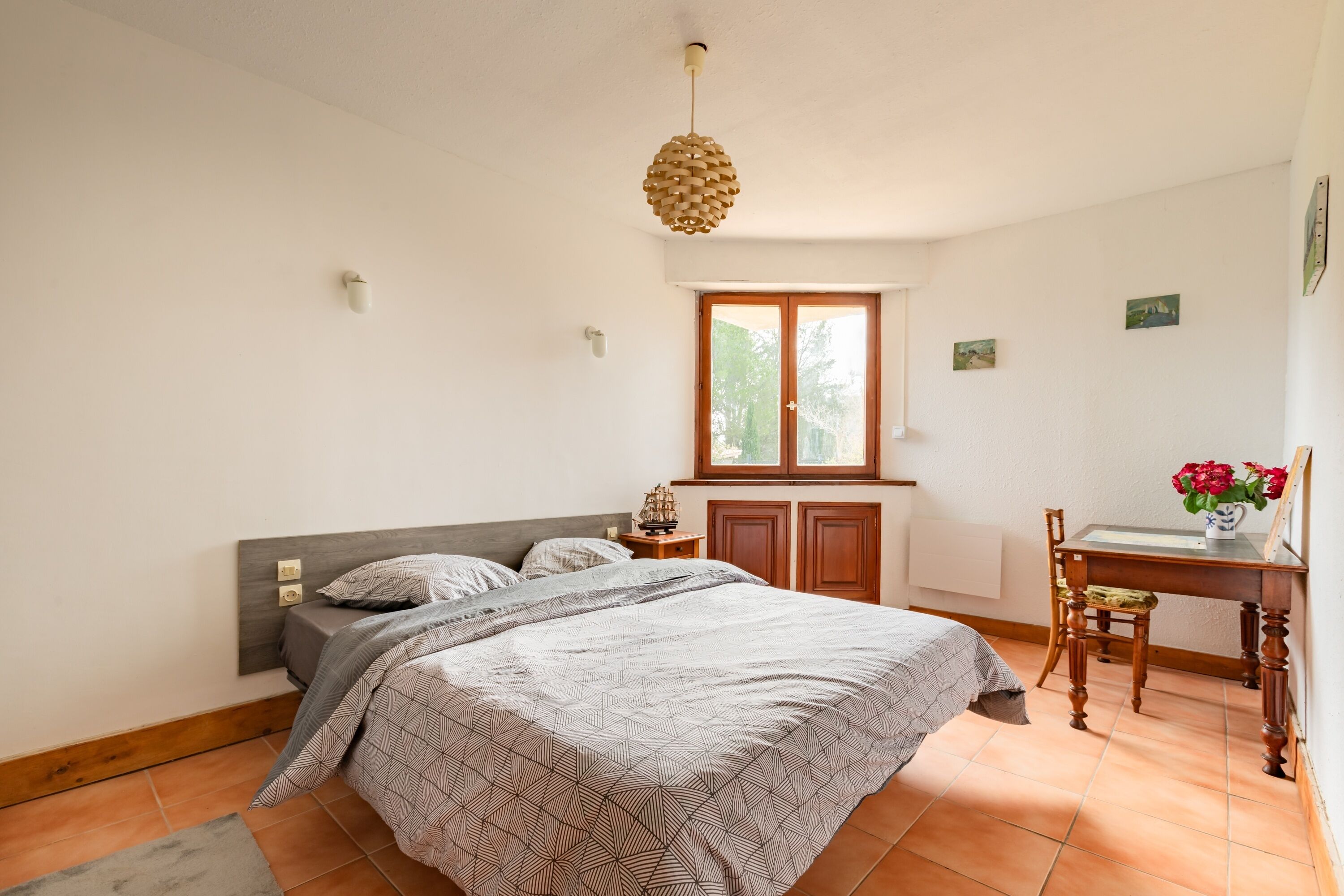 A bedroom with a bed, a desk, and a window.
