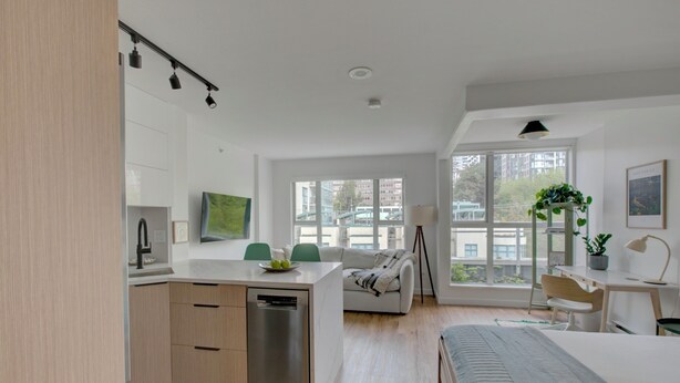Una cocina moderna con lavavajillas, un comedor con sofá y un amplio ventanal con vistas a edificios.