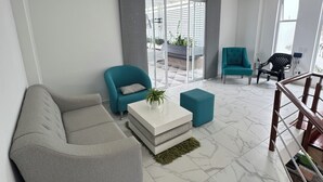 Una sala moderna con un sofá seccional gris, sillones azul verdosos, una mesa de centro blanca y una escalera que conduce a un nivel superior.