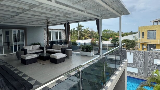 Un espacio exterior moderno con barandilla de cristal, mobiliario de exterior y piscina.
