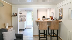 A modern kitchen with a dining area, featuring a kitchen island, two bar stools, and a sofa with a cushion.