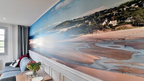 Una habitación con un gran mural de playa en la pared, un sofá, una mesa de comedor con un jarrón de flores y una ventana con cortinas.