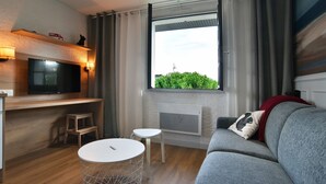 Un salón moderno con un sofá gris, un televisor de pantalla plana, una mesa redonda pequeña y una ventana con vistas a zonas verdes.