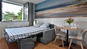 Habitación compacta con cama, una mesita pequeña y una silla. Un ventanal grande ofrece vistas al exterior.