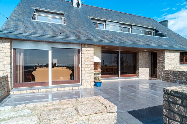 A modern house with a stone facade, large sliding glass doors, and a tiled patio.