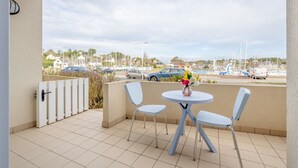 Un balcón con dos sillas y una mesa, con vistas a un puerto deportivo con barcos y coches.