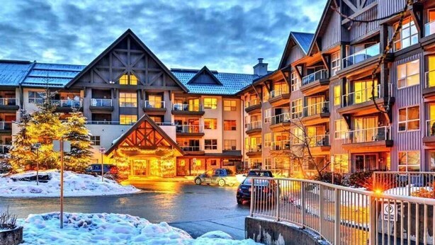 A multi-story hotel with a ski lodge entrance, balconies, and a covered parking area. - John's Aspens Ski In/Out (Whistler)