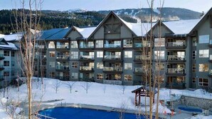 A multi-story hotel with a pool area, surrounded by snow-covered landscape and mountains. - John's Aspens Ski In/Out (Whistler)