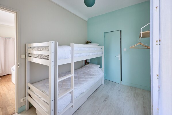 A bunk bed room with a light blue wall, a door, and a wooden floor.