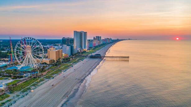 A coastal cityscape with a beach, a Ferris wheel, and high-rise buildings during sunset.