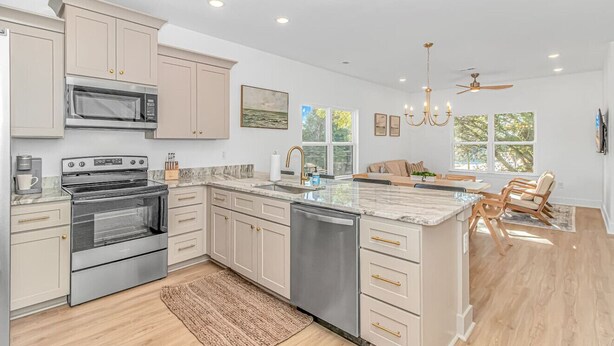 A modern kitchen with a central island, stainless steel appliances, and a dining area with wooden chairs. - 4BR Beach Oasis w/ Private Pool! 1000 ft from the water (Myrtle Beach)