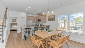 A modern kitchen with a central island, wooden dining table with chairs, and a view of the outside through large windows. - 4BR Beach Oasis w/ Private Pool! 1000 ft from the water (Myrtle Beach)