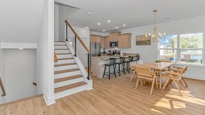 A modern kitchen with wooden flooring, a dining area with wooden furniture, and a staircase with a glass railing. - 4BR Beach Oasis w/ Private Pool! 1000 ft from the water (Myrtle Beach)