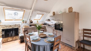 A cozy kitchen with a dining area set for four, featuring a stone wall, wooden cabinets, and a large window. - Rêve Emeraude - 100m de la Plage (Cancale)