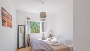 Un dormitorio con cama, ventana con cortinas, lámpara colgante y vista a zonas verdes.