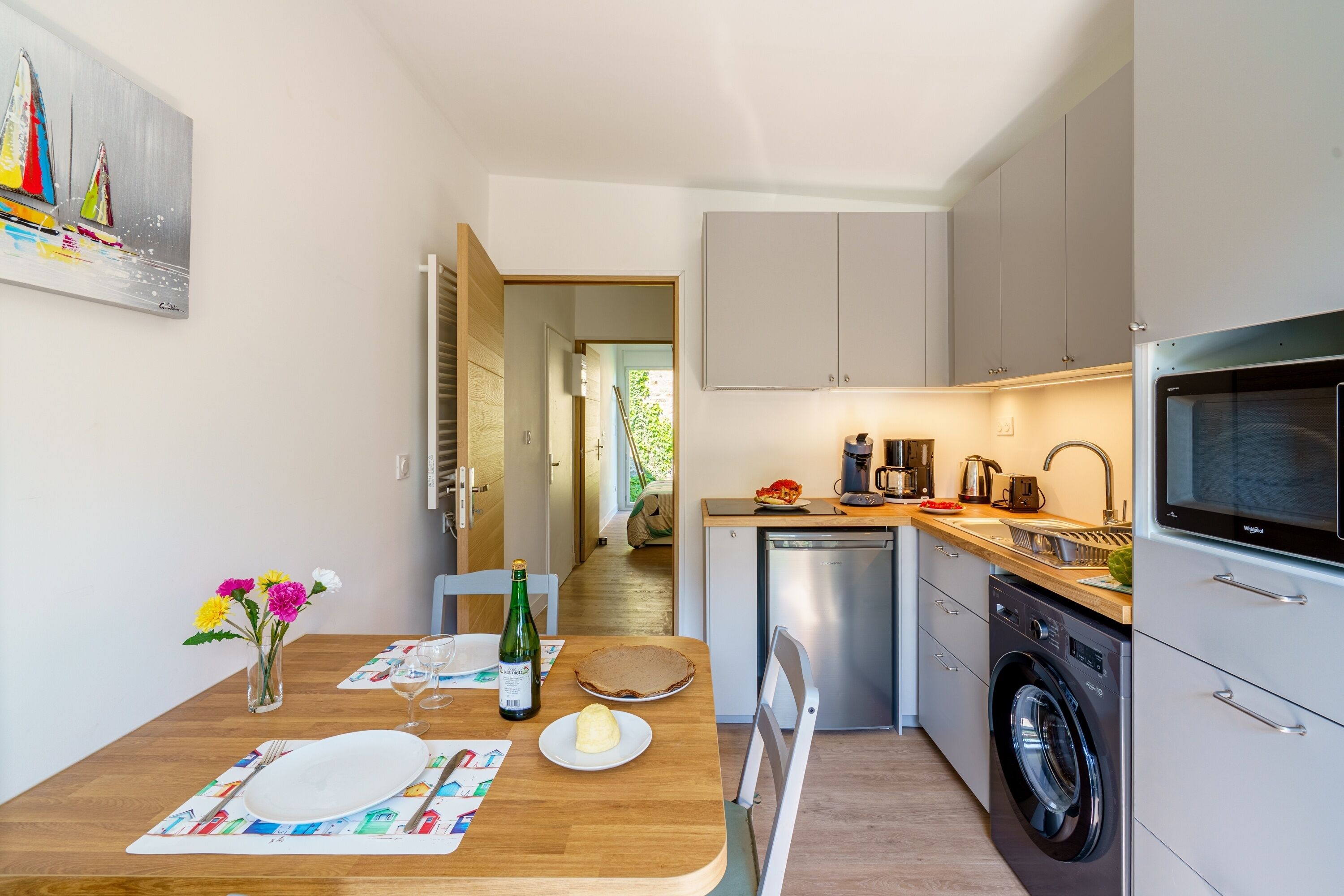 Una cocina moderna con una mesa de comedor de madera dispuesta para dos personas, una lavadora y un microondas.