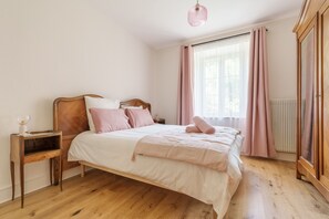 A bedroom with a wooden bed, a nightstand, a radiator, and a wardrobe. - Gîte de l'Oriel - Gîte avec Grand Jardin (Sainte-Marie-aux-Mines)