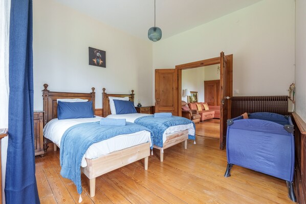 A room with two wooden beds, a blue chair, and a wooden door leading to another room.