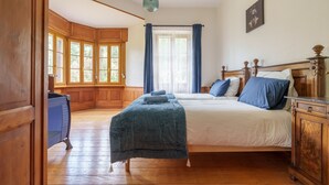 Un dormitorio con piso de madera, una cama con ropa de cama azul, un armario de madera y una ventana con cortinas.