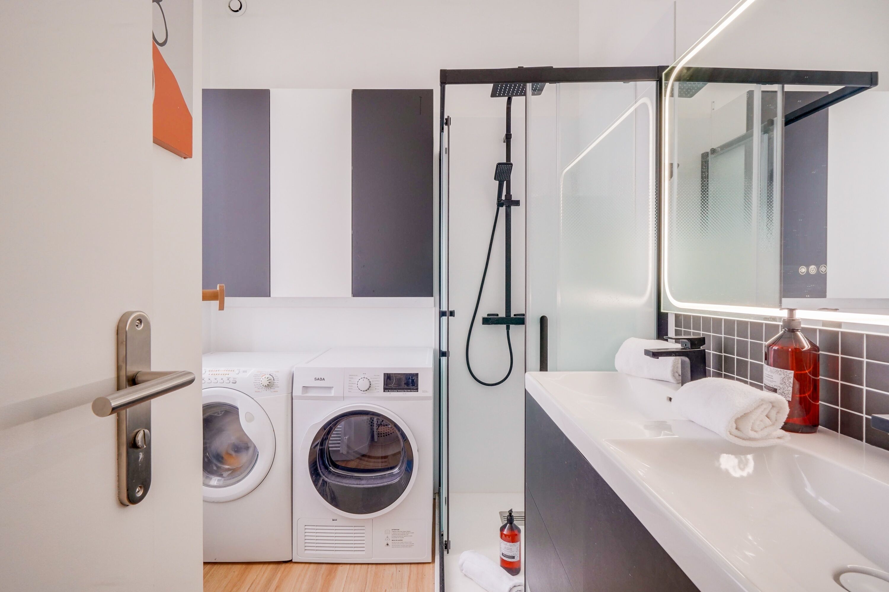 A modern bathroom with a washing machine, a shower, and a sink with a mirror.