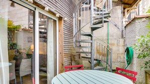 Une terrasse extérieure avec une table ronde et des chaises rouges, un escalier en colimaçon et une vue sur la rue.