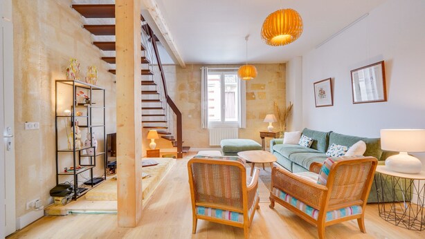 Un vaste espace de vie comprenant un escalier, des meubles en osier et un canapé vert.