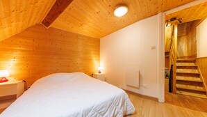 Un dormitorio con techo de madera, una cama, una mesita de noche con lámpara y una escalera que sube a otro nivel.