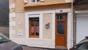Un edificio con fachada color beige, una puerta de madera y una ventana con mantel a cuadros.