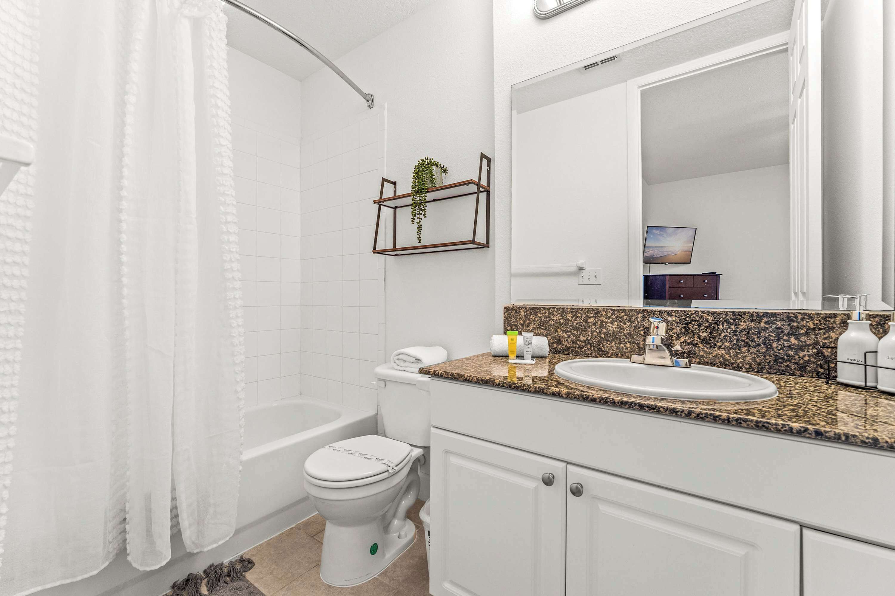 A modern bathroom with a white toilet, a sink, and a bathtub. There is a towel rack with a plant on the wall, and a mirror above the sink.