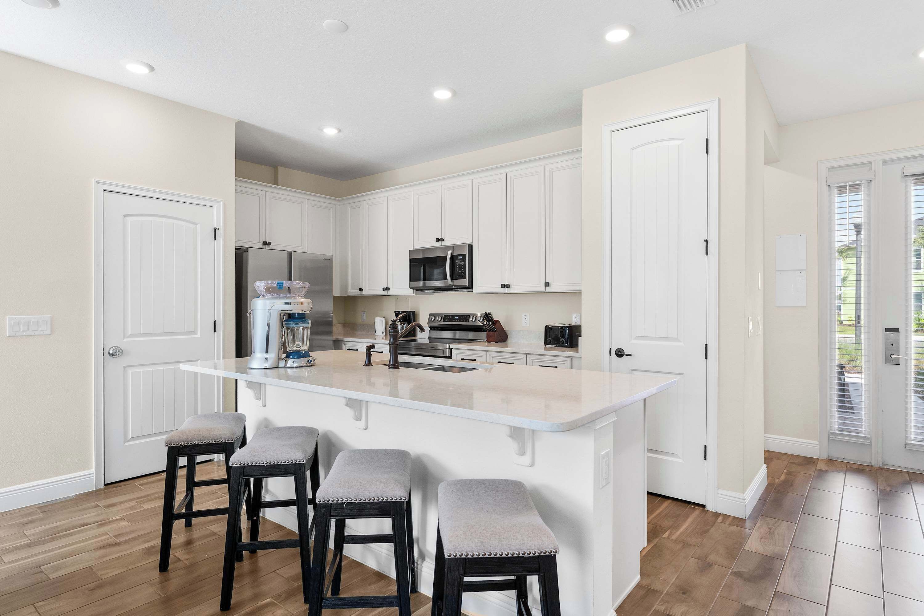 A kitchen with white cabinets, a central island with stools, and a stainless steel refrigerator.