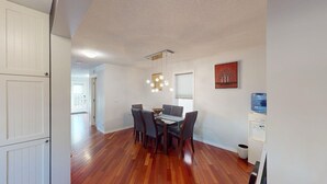 A dining area with a wooden floor, a table with chairs, a hanging light fixture, and a water dispenser. - Cozy&comfy family size house. Beautiful location, near COP. Pet friendly &Clean. (Calgary)