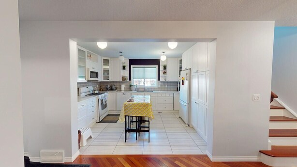 A modern kitchen with white cabinets, a central island, and a dining table with a yellow tablecloth. - Cozy&comfy family size house. Beautiful location, near COP. Pet friendly &Clean. (Calgary)