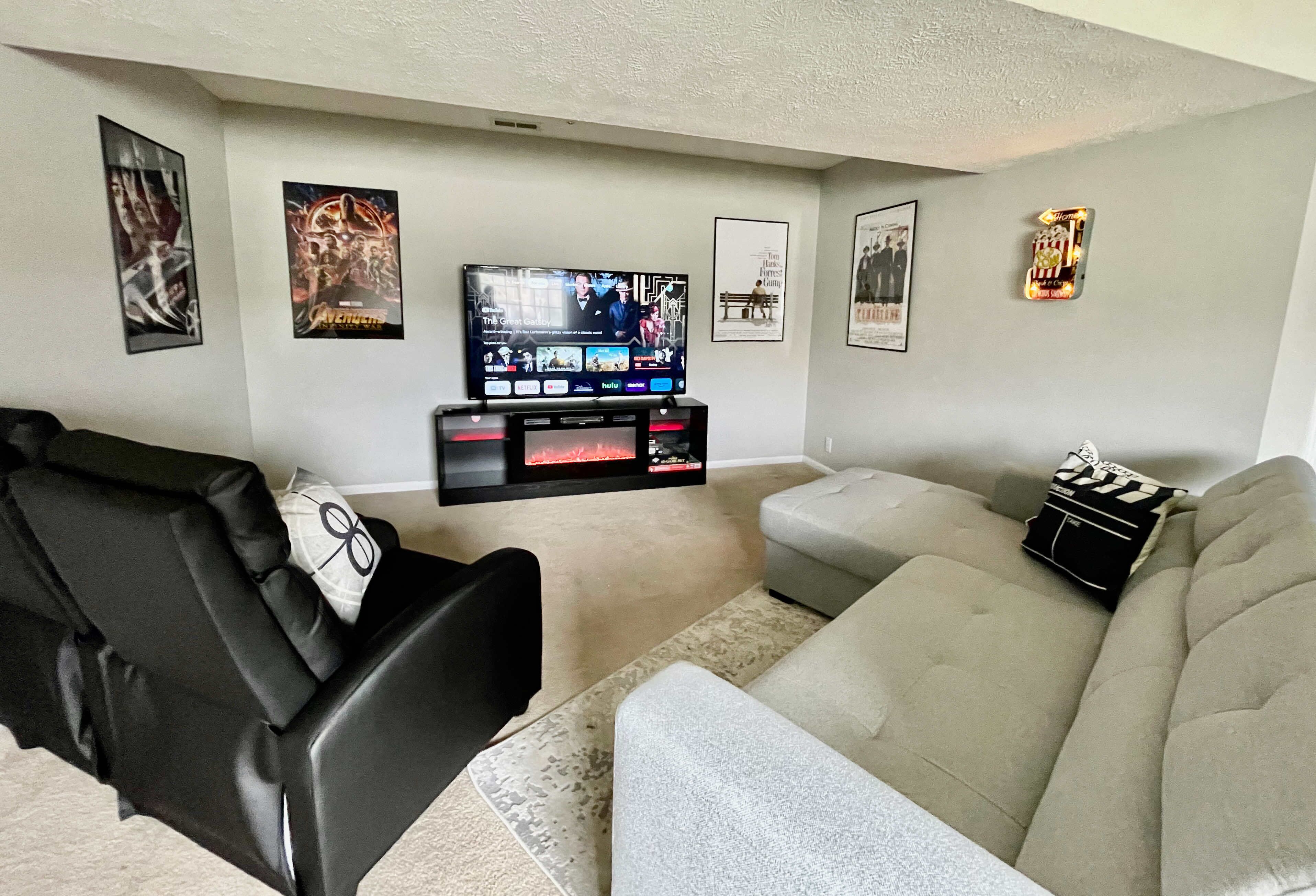 A living room with a black leather sofa, a grey couch, and a flat-screen TV on a stand.